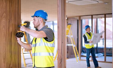 A construction worker with a drill and another with a construction project