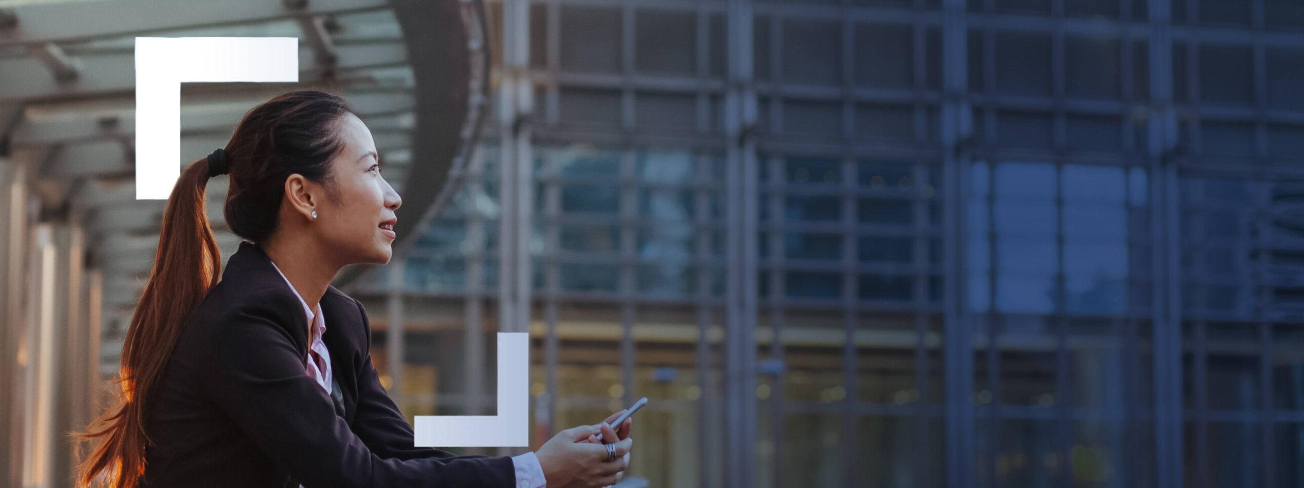 A woman holding a phone looking into the distance with a smile